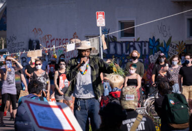 George Floyd Square garden caretaker Jay Webb speaks with those gathered at a rally at George Floyd Square on the day that President Trump was in town.