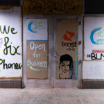 Cell phone store open for business with boards on the windows.