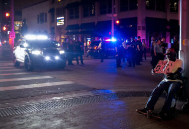 A homeless man sits on Nicollet Mall asking for help while riot police move in after rioting broke out following the false rumors of a downtown shooting by the police. The man died of a suicide.