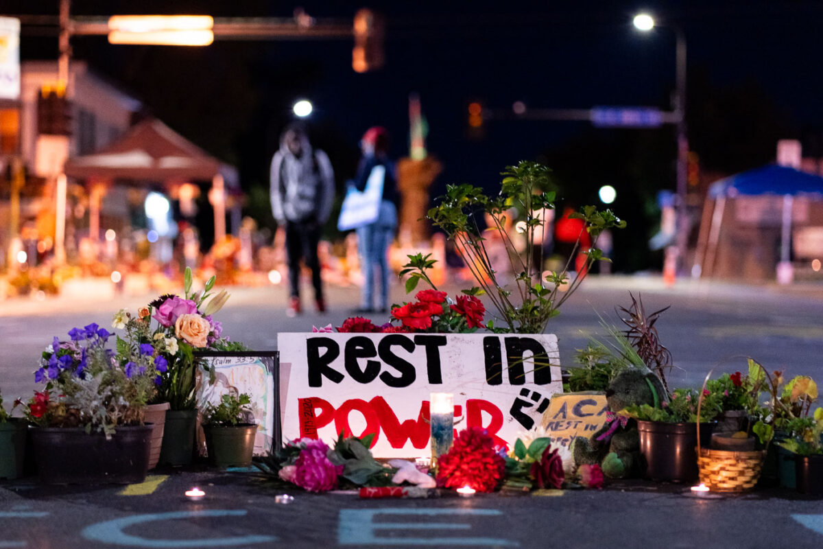 A memorial on Chicago Avenue in Minneapolis near the location of George Floyd's death with lit candles. A sign reads “Rest In Power”.