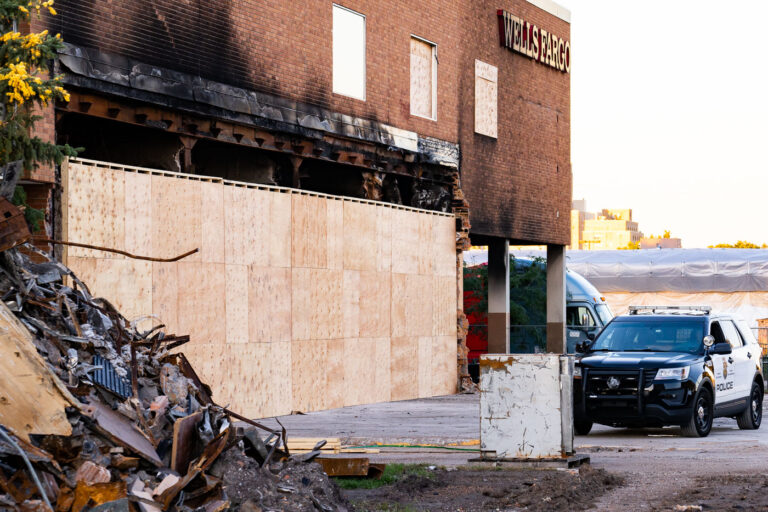 Fire Damaged Wells Fargo with Minneapolis Squad Car 3 A Minneapolis Police Officer stands guard at the former Wells Fargo Bank in Minneapolis. The building was burned during protests following the May 25th, 2020 death of George Floyd. The security was 24/7 while the bank looked for a way to safely allow people into the building to retrieve the items in their safety deposit boxes.