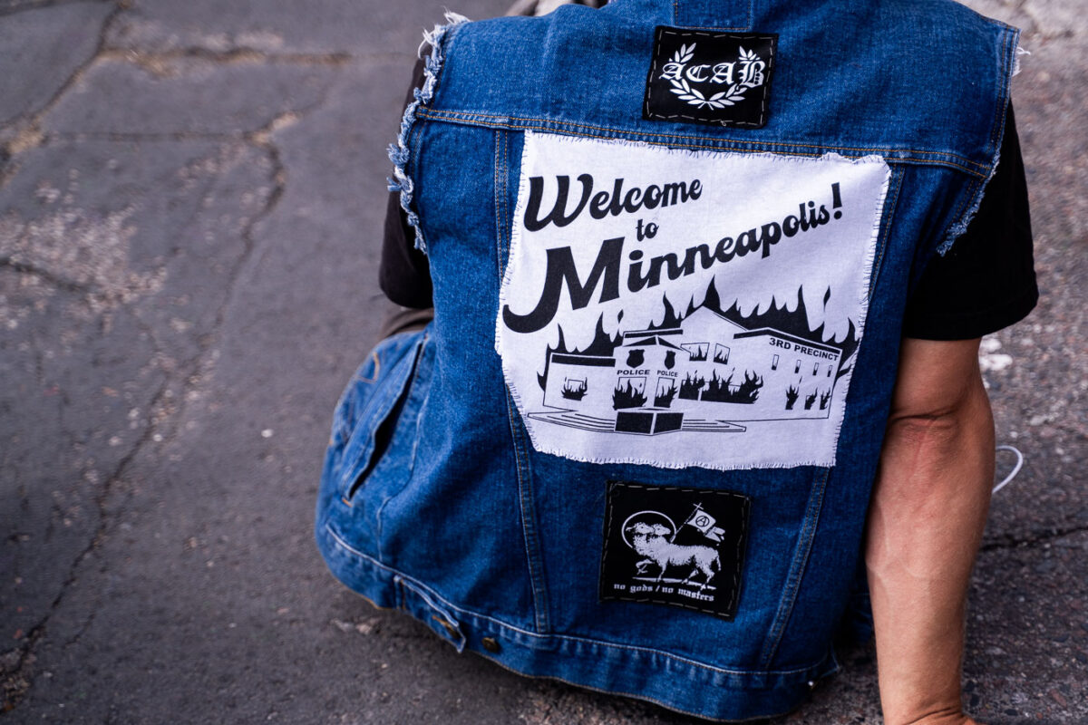 A man wears a jacket with a “large Welcome to Minneapolis" patch.