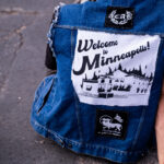 A man wears a jacket with a “large Welcome to Minneapolis" patch.