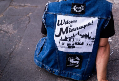 A man wears a jacket with a “large Welcome to Minneapolis" patch.