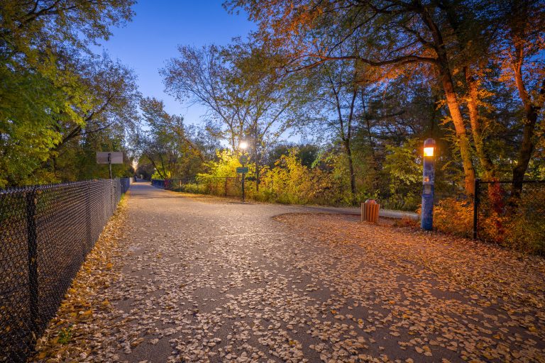 Illuminated path through the Midtown Greenway in Minneapolis lined with autumn trees at dusk.