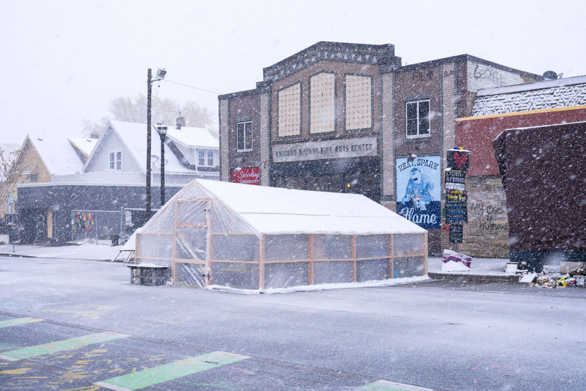 As the first snowfall falls, a recently built greenhouse is enclosed to keep plants safe during the cold months at George Floyd Square.