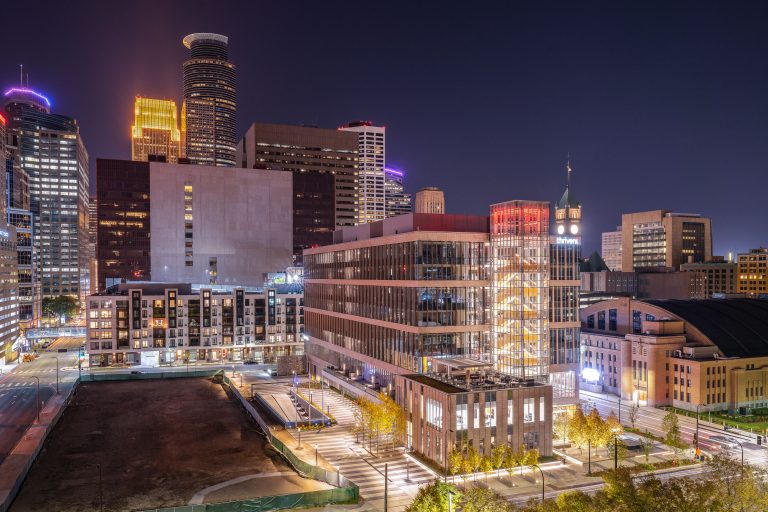 The illuminated Thrivent building at night in downtown Minneapolis, surrounded by other high-rise office and residential towers.