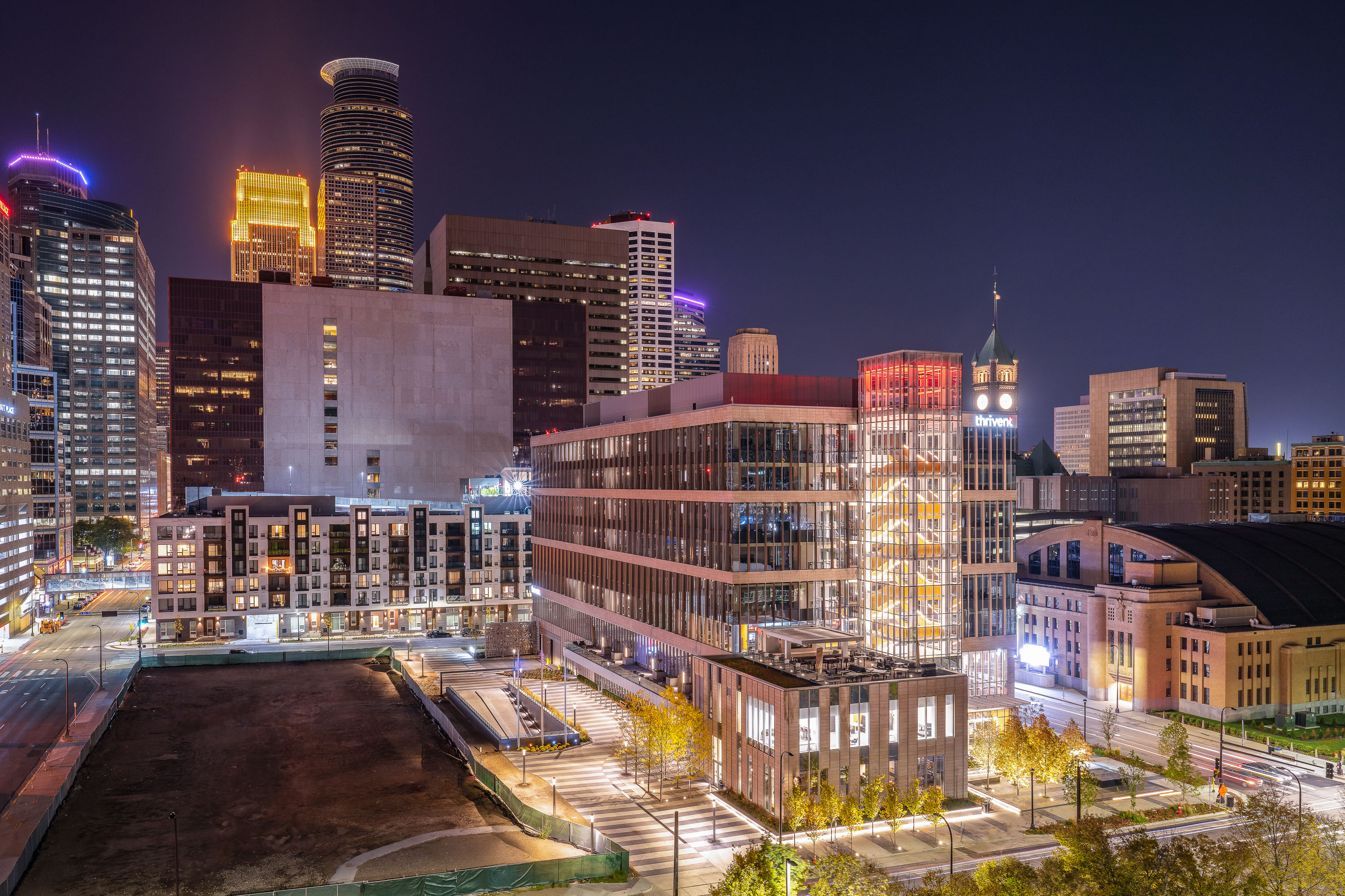 The illuminated Thrivent building at night in downtown Minneapolis, surrounded by other high-rise office and residential towers.