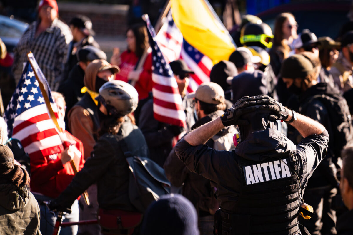 A man with an ANTIFA patch on the back of his vest at a Stop The Steal rally with Proud Boys.