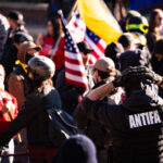 A man with an ANTIFA patch on the back of his vest at a Stop The Steal rally with Proud Boys.