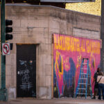 An artist stops to talk with someone as he paints a mural on Lyndale Avenue storefront boards.