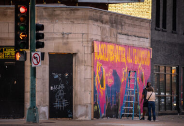 An artist stops to talk with someone as he paints a mural on Lyndale Avenue storefront boards.
