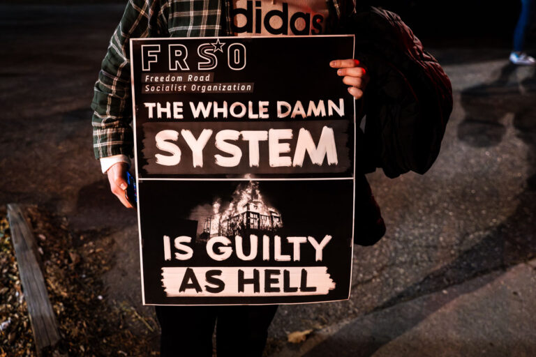 Protest Sign Declaring “The Whole Damn System Is Guilty as Hel 2 A protester holds up a sign by the Freedom Road Socialist Organization (FRSO). It reads “The whole damn system is guilty as hell”.