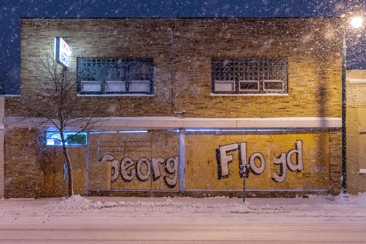 Storefront boards reading "George Floyd" on Lake Street during snowfall.