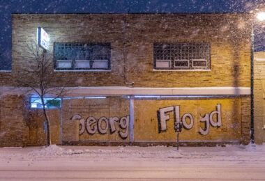 Storefront boards reading "George Floyd" on Lake Street during snowfall.