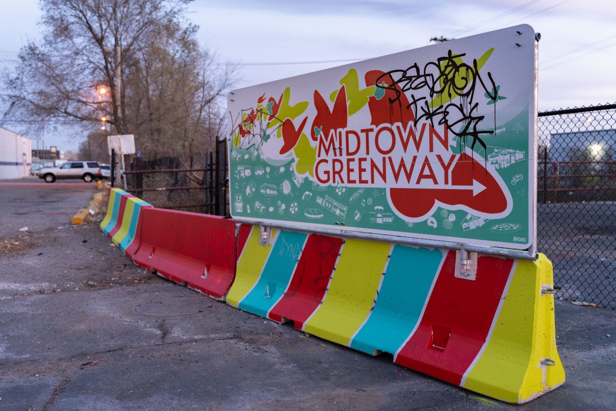 A Midtown Greenway sign with colorful striped barriers blocks vehicle access at Nicollet Avenue in South Minneapolis.