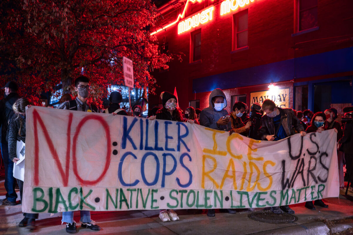 Protesters hold up a large banner reading “No Killer Cops Ice Raids US Wars” prior to a march that would eventually end with 646 people arrested on Interstate 94.