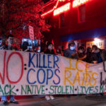 Protesters hold up a large banner reading “No Killer Cops Ice Raids US Wars” prior to a march that would eventually end with 646 people arrested on Interstate 94.