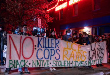 Protesters hold up a large banner reading “No Killer Cops Ice Raids US Wars” prior to a march that would eventually end with 646 people arrested on Interstate 94.