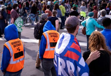 Protesters gather outside of the Minneapolis Police Third Precinct as part of a march shortly after Biden won the Presidential election. Protesters wearing orange vests that read “Democracy Defender”.