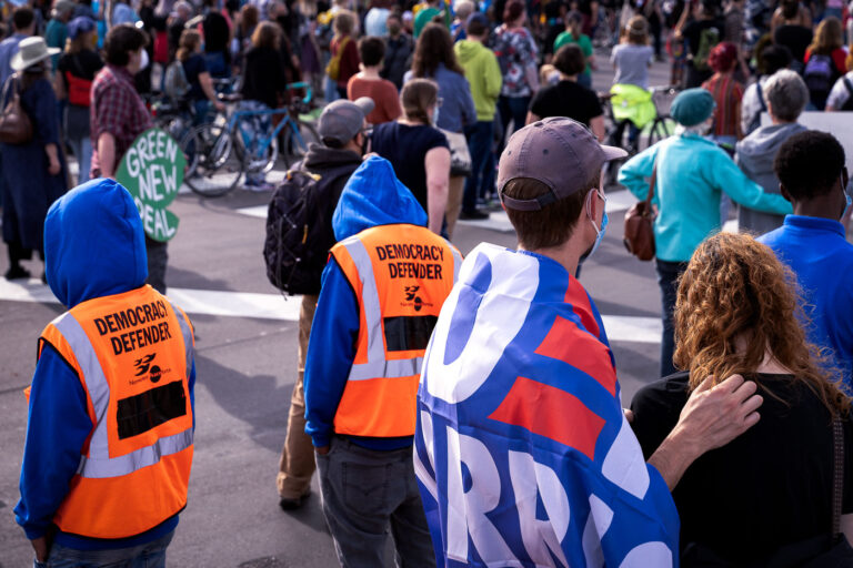 Democracy Defenders 2 Protesters gather outside of the Minneapolis Police Third Precinct as part of a march shortly after Biden won the Presidential election. Protesters wearing orange vests that read “Democracy Defender”.