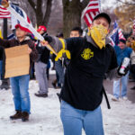 A man wearing a "Proud Boys" shirt waves a flag at a pro-Trump rally outside the Minnesota Governor's mansion following President Trump's re-election loss.