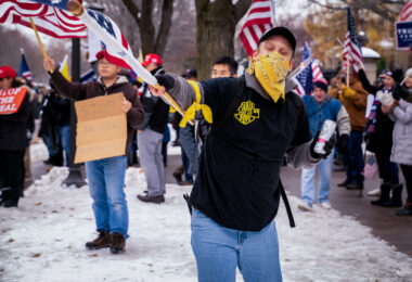 A man wearing a "Proud Boys" shirt waves a flag at a pro-Trump rally outside the Minnesota Governor's mansion following President Trump's re-election loss.