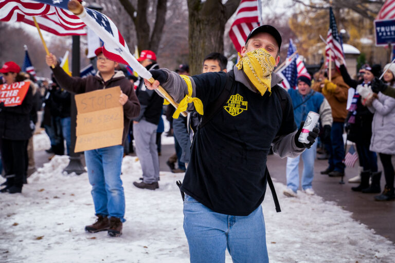 Proud Boy at Governor's Mansion 1 A man wearing a "Proud Boys" shirt waves a flag at a pro-Trump rally outside the Minnesota Governor's mansion following President Trump's re-election loss.