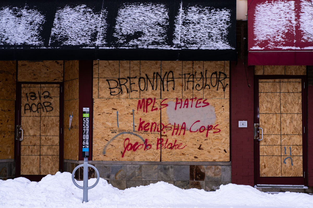 Boards on a building near the burned Minneapolis Police third precinct with "Breonna Taylor", "Mpls Hates Kenosha Cops", "Jacob Blake", "1312" and "ACAB" written on them.