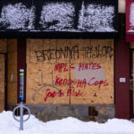 Boards on a building near the burned Minneapolis Police third precinct with "Breonna Taylor", "Mpls Hates Kenosha Cops", "Jacob Blake", "1312" and "ACAB" written on them.