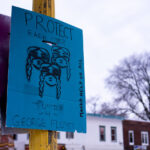 A sign at George Floyd Square that reads "Protect Each Other" "Justice 4 George Floyd" "Masks Help Us All"
