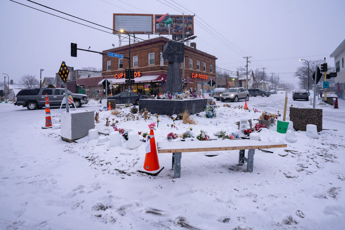 Snow falls over the metal fist at George Floyd Square.