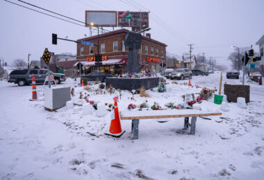 Snow falls over the metal fist at George Floyd Square.