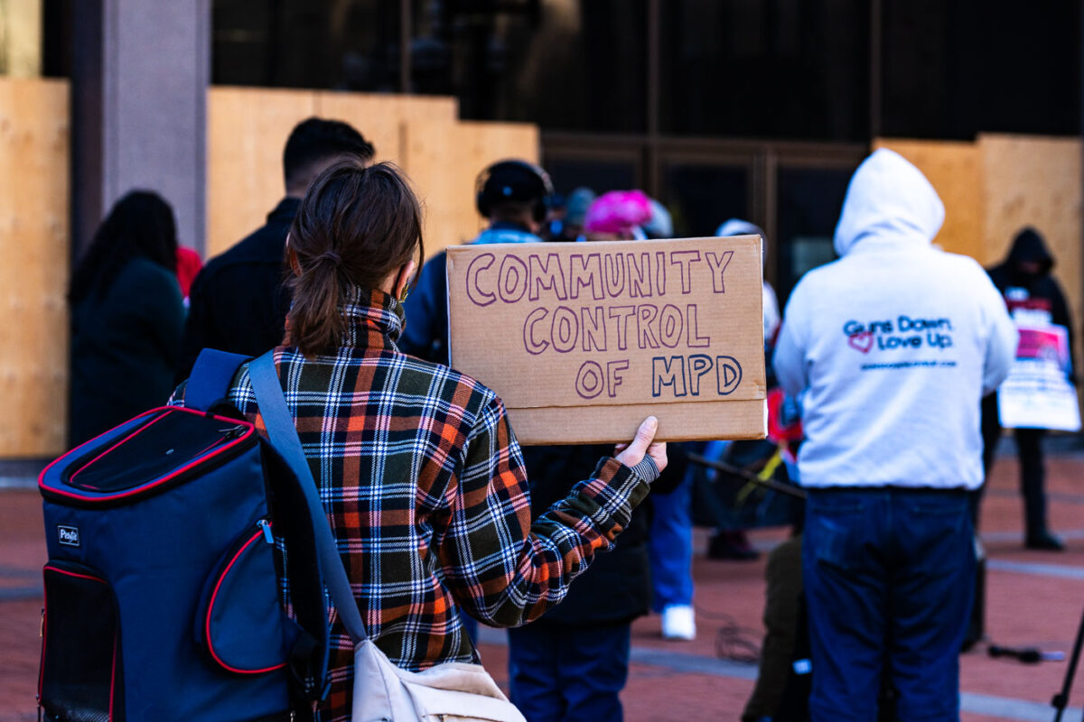 A woman holds a sign at a press conference announcing a March 8th protest at the start of the Derek Chauvin trial.