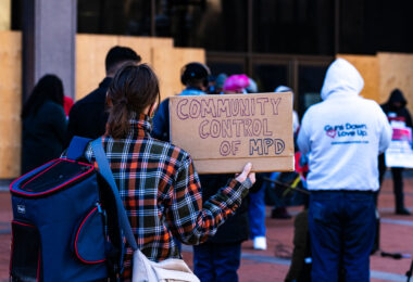 A woman holds a sign at a press conference announcing a March 8th protest at the start of the Derek Chauvin trial.