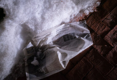 A wet newspaper lays in the snow outside the Hennepin County Government Center. Article titled “Who’s running for Mayor of Minneapolis?”