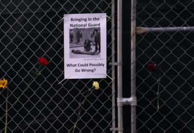A sign hanging on a fence around the Hennepin County Government Center that reads "Bringing in the National Guard. What could possibly go wrong?".