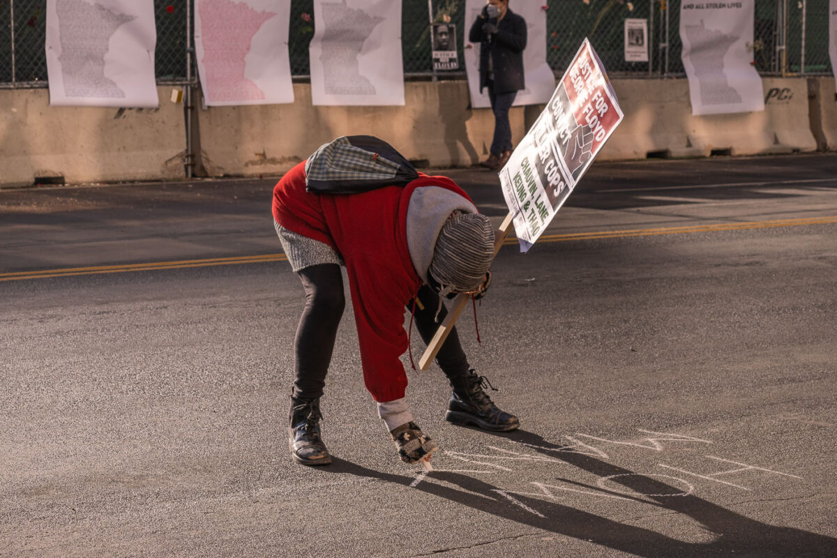 A protester writes with chalk outside the Hennepin County courthouse at the start of the Derek Chauvin murder trial.