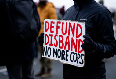 A woman holds up a sign that reads "Defund Disband No More Cops" outside the Brooklyn Center Police Department.