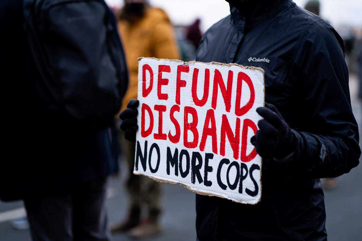 A woman holds up a sign that reads "Defund Disband No More Cops" outside the Brooklyn Center Police Department.