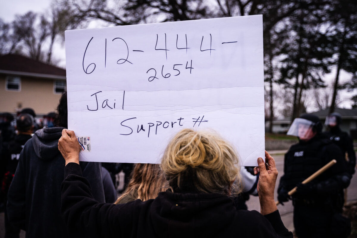 A woman holds up a sign with the number for the National Lawyers Guild.