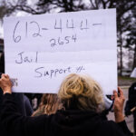 A woman holds up a sign with the number for the National Lawyers Guild.