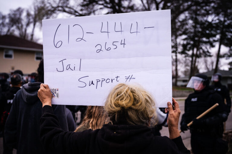Protester holds up a jail support number 1 A woman holds up a sign with the number for the National Lawyers Guild.