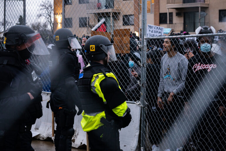 Protesters yell at police through fence in Brooklyn Center 4 Protesters and police officers with fencing in between them.