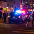 Bar patrons walk down Hennepin Avenue past armed Minneapolis police who responded to those protesting the June 3rd shooting death by a Federal task force.