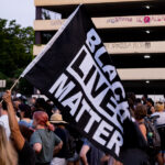 Protester holds up Black Lives Matter flag while marching down Lake Street during a march following the June 3rd and June 13th deaths of Winston Smith and Deona Marie.Winston Smith was killed after Hennepin and Ramsey County officers fired their weapons while part of a Federal Task Force serving a warrant. Deona Marie was killed when Nicholas Kraus drove his vehicle into those protesting the killing of Smith.
