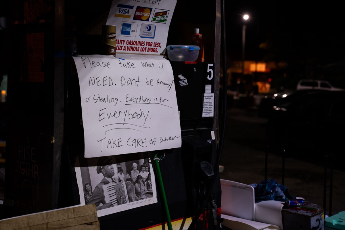 A sign at George Floyd Square reading "Please take what u need, don't be greedy or stealing. Everything is for everybody. Take care of each other"