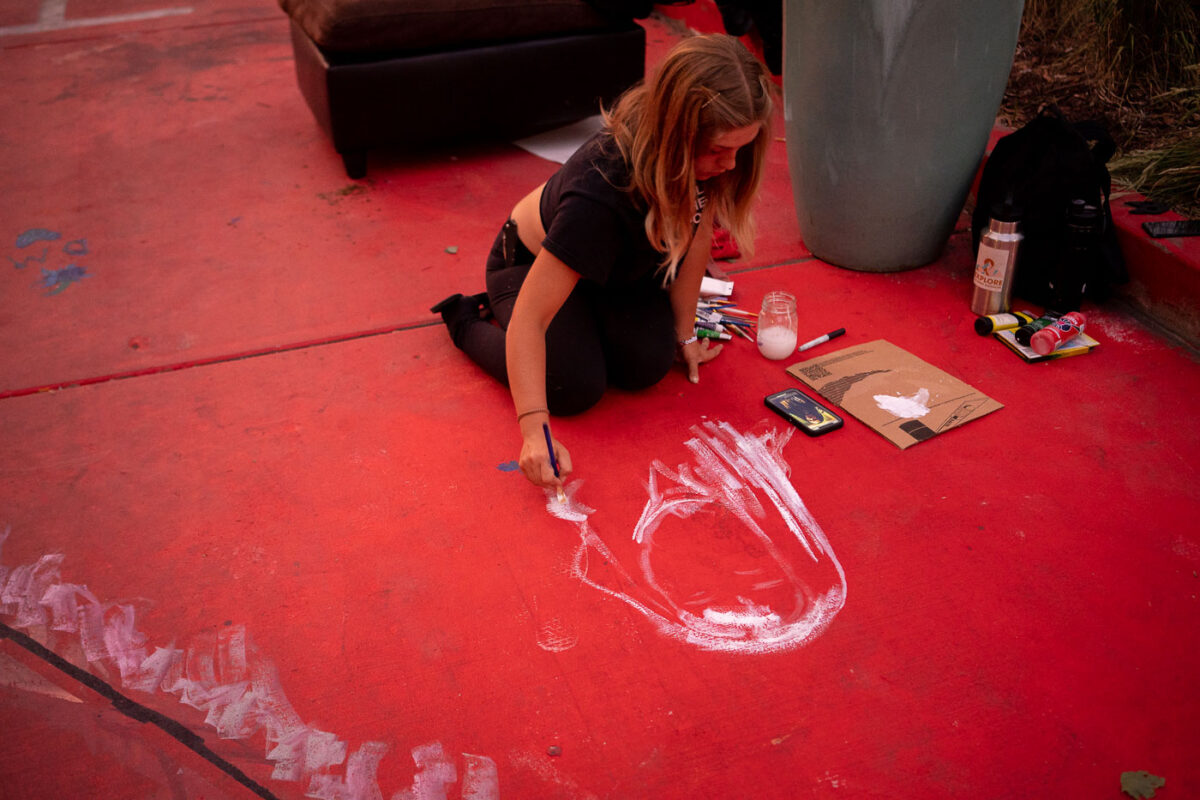 An artist draws Winston Smith on the pavement outside the parking garage where Winston Smith was killed by law enforcement on June 3rd.