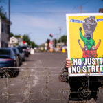 Protester holds up sign at George Floyd Square street barricade 3 A woman holds a "No Justice No Streets" yard sign on the day the city tried to clear out barricades around the square.