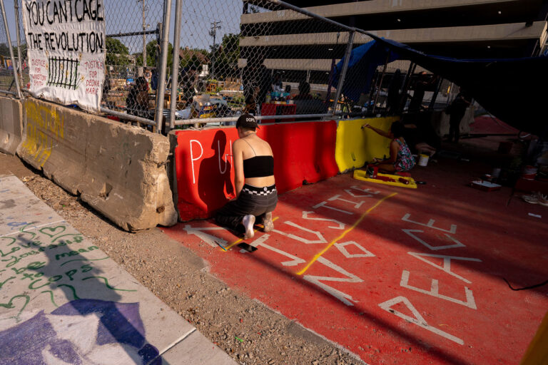 Protester writes on barricades in Uptown Minneapolis 3 Protesters paint the concrete barriers around a peace garden built by those protesting the June 3rd and June 13th deaths of Winston Smith and Deona Marie.Deona Marie was killed when Nicholas Kraus drove his vehicle into those protesting the killing of Winston Smith.Winston Smith was killed after Hennepin and Ramsey County officers fired their weapons while part of a Federal Task Force serving a warrant.